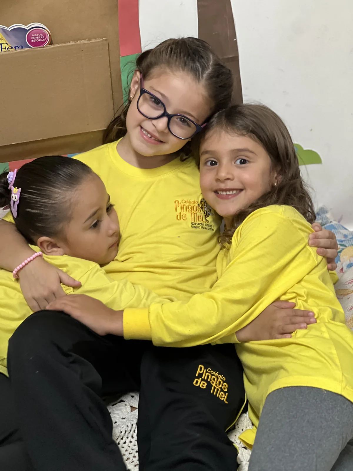 Três meninas abraçadas com uniforme amarelo